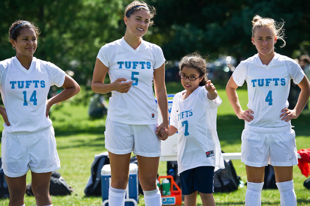 有三名妇女学院足球运动员的一个小女孩在比赛。由于Tufts Alums共同创立的团队影响，严重疾病的儿童与大学运动队相匹配，带来了属于孩子们的透视