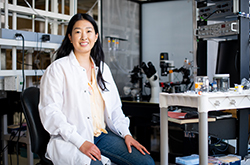 实验室外套的一个女人坐在实验室里。Noell Cho，生物医学科学研究生院博士学生，导师其他第一代大学生，太平洋岛民和科学妇女。