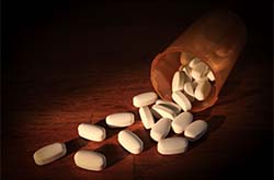 一个开着的瓶子洒出白色的药丸在桌子上。塔夫茨大学对10个州的评估确定了过量死亡风险最大和最需要服务的社区。